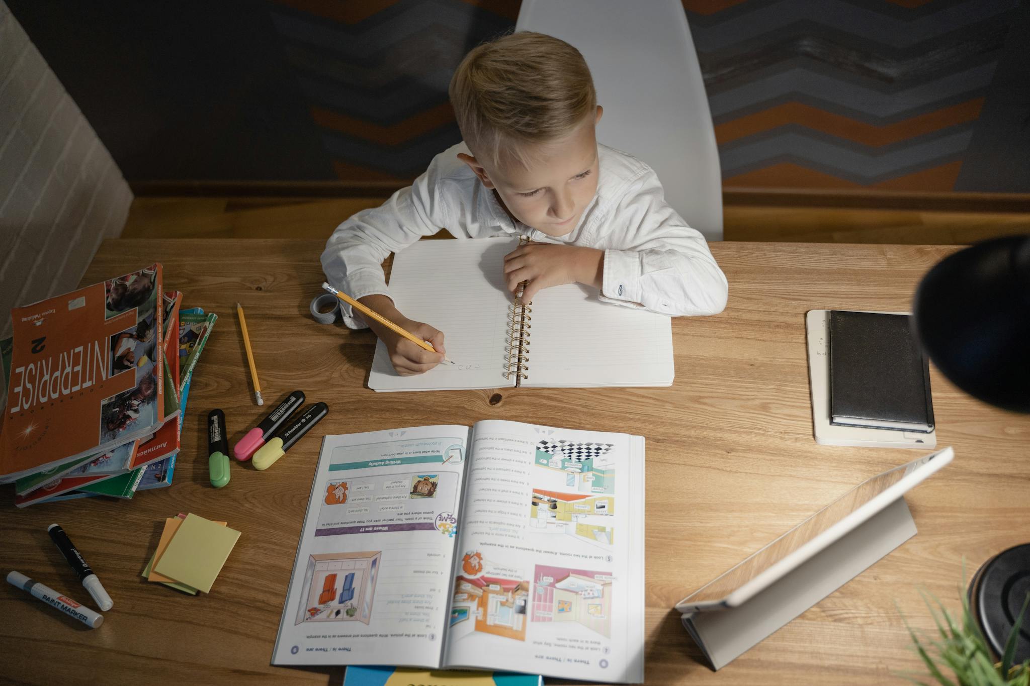 A young boy studying at a desk with books and a tablet, highlighting modern education methods.