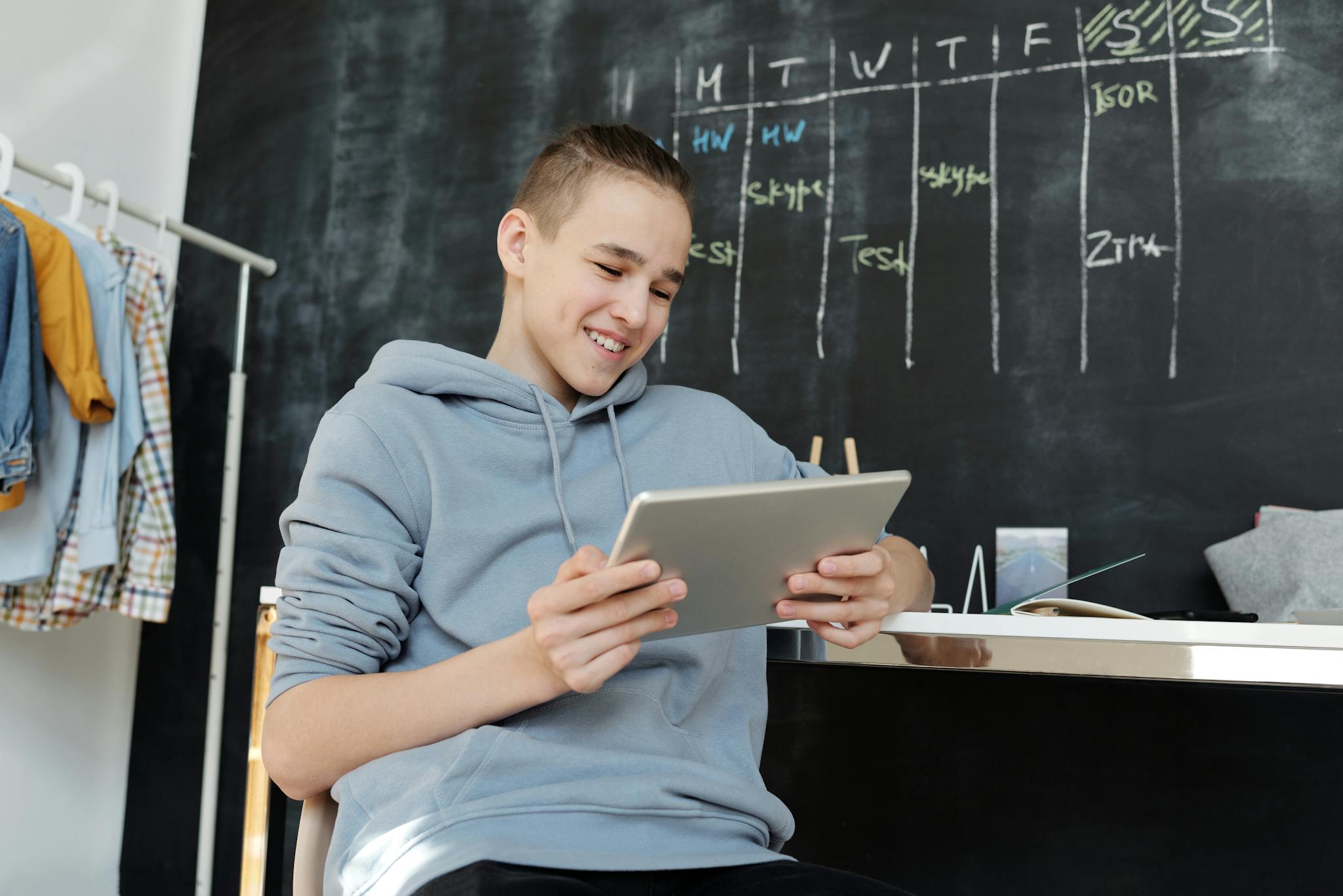 Teen sitting indoors, smiling while using a tablet. Relaxed classroom vibe.